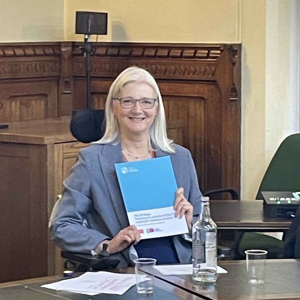 A picture of Catherine Hale holding a report in a parliamentary room