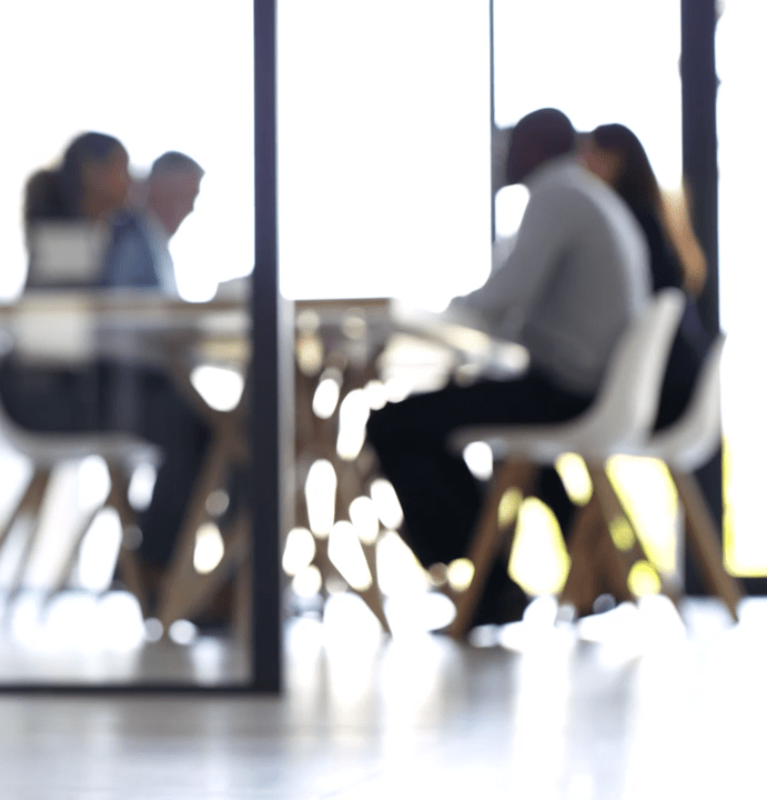 A blurry image of a group of workers in a meeting behind a screen